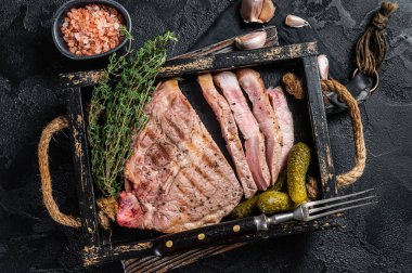 Ahşap tepside otlarla pişirilmiş ızgara domuz bifteği. Siyah arka plan. Üst görünüm