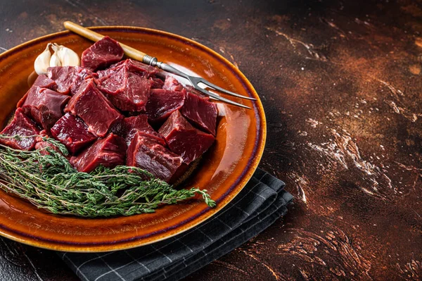 Cut Beef or veal raw heart in a rustic plate with herbs. Dark background. Top View. Copy space