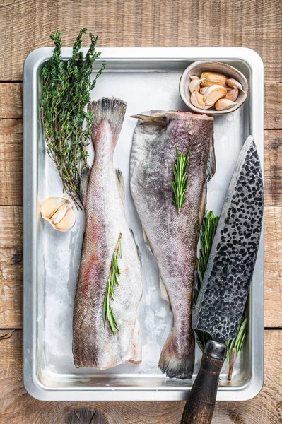 Rå torsk hel fisk i stål kök bricka med timjan och rosmarin. Trä bakgrund. Ovanifrån — Stockfoto