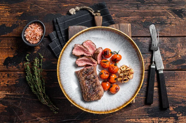 Carne de lombo de cordeiro assada em prato com tomate grelhado e alho, filé de lombo de carneiro. Fundo escuro. Vista superior — Fotografia de Stock