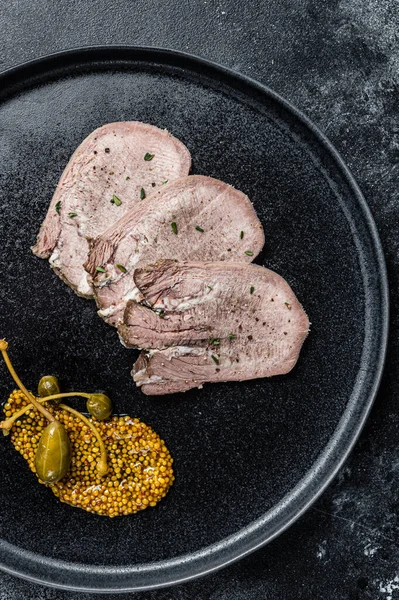 Bir tabakta haşlanmış dil dilimleri. Siyah arka plan. Üst görünüm