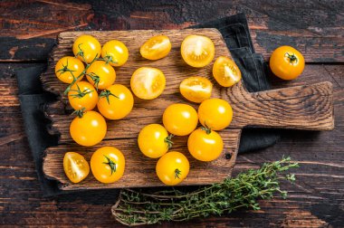 Tahta kesme tahtasına dilimlenmiş sarı kiraz domatesi. Koyu ahşap arka plan. Üst görünüm