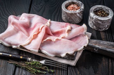 Tahtada otlarla dilimlenmiş jambon. Siyah ahşap arka plan. Üst görünüm