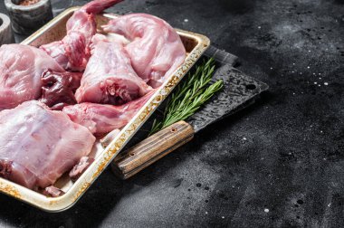 Çiğ yaban tavşanı, bacaklar, çelik tepside taze et ve bitki. Siyah arka plan. Üst Manzara. Boşluğu kopyala