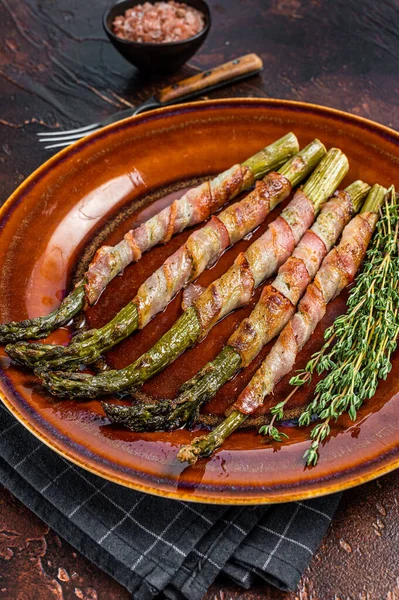 Gegrillter grüner Spargel in Speckmantel auf einem Teller. Dunkler Hintergrund. Ansicht von oben — Stockfoto