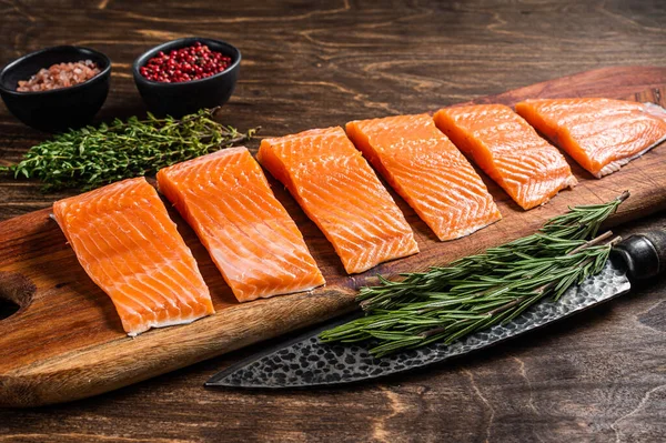 Sliced salmon fillet, raw fish meat with thyme and rosemary. Wooden background. Top view — Foto Stock