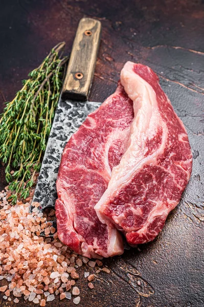 Prime Black Angus beef steaks Raw Striploin or New York on a butchery meat cleaver. Dark background. Top view