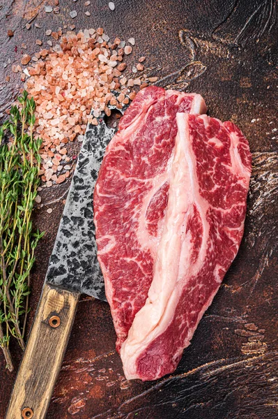 Prime Black Angus beef steaks Raw Striploin or New York on a butchery meat cleaver. Dark background. Top view
