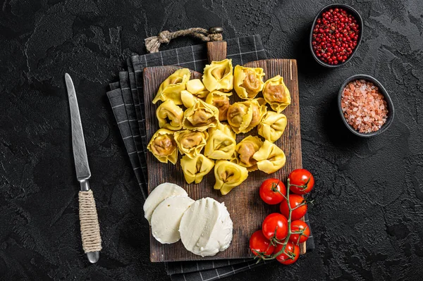 Mozzarella peyniri ve domatesli çiğ ravioli. Siyah arka plan. Üst görünüm
