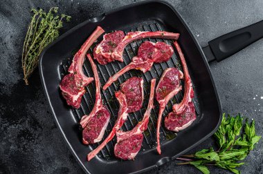 Çiğ kuzu eti, tavada kuzu pirzolası ve otlar pişmeye hazır. Siyah arka plan. Üst görünüm