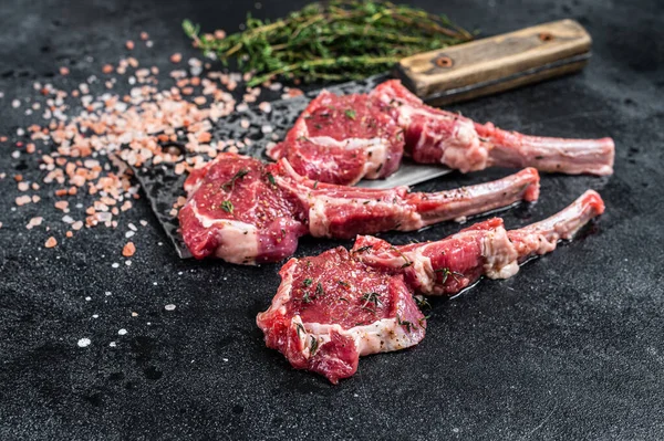 Raw uncooked lamb mutton meat chops steaks on a butcher cleaver. Black background. Top view