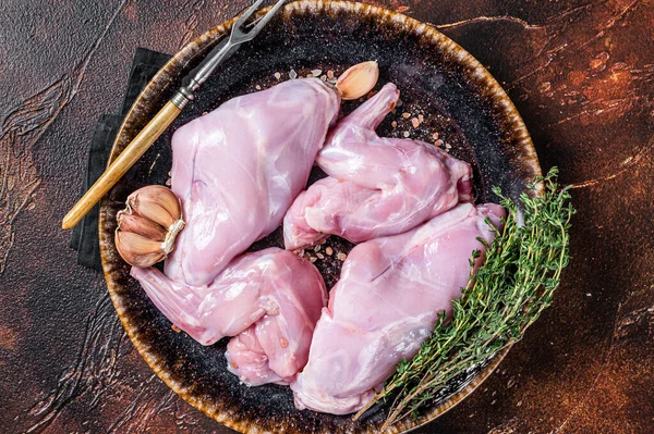 Pernas de coelho frescas cruas em uma chapa com ervas. Fundo escuro. Vista superior — Fotografia de Stock