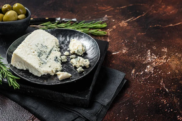 Wedge of Roquefort cheese in a steel plate with olives and herbs. Dark background. Top view. Copy space — стоковое фото