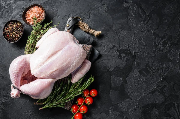Uncooked raw whole chicken on wooden board with thyme and rosemary. Black background. Top view. Copy space