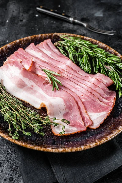 Rå skivad bacon redo för matlagning med örter. Svart bakgrund. Ovanifrån — Stockfoto