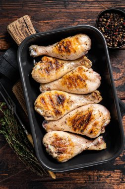 Pişmiş tavuk budu budu, otlarla dolu bir kabın içinde. Ahşap arka plan. Üst görünüm