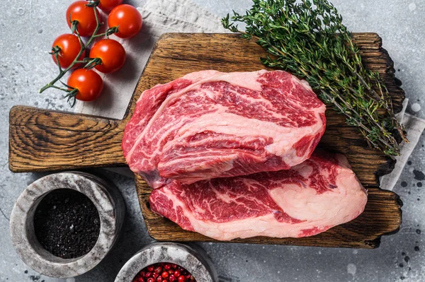 Raw Chuck Roll beef meat steaks on a wooden board with thyme. Gray background. Top view — Stockfoto