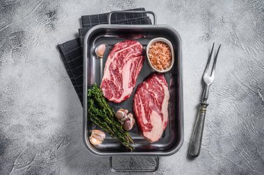 Çelik mutfak tepsisinde pişmemiş çiğ çiğ göz yuvarlama bifteği. Gri arka plan. Üst görünüm