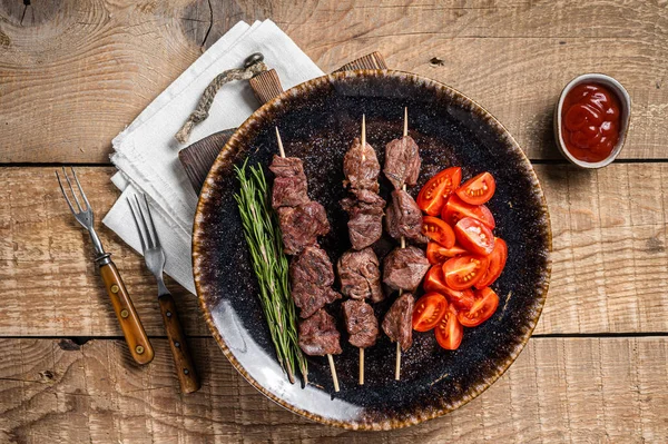 Grilled Beef veal shish kebab Skewers or Shashlik in a plate with tomato. Wooden background. Top view — Stockfoto