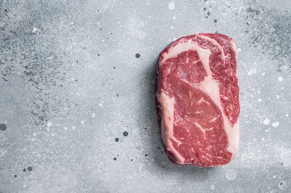生のリブアイステーキ、肉屋の板の上の牛肉の霜降り肉。灰色の背景。最上階だ。スペースのコピー — ストック写真