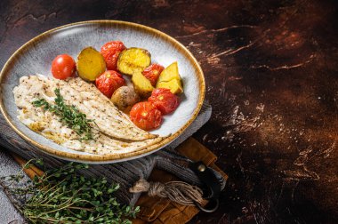 Kavrulmuş Pollock balığı filetosu, garnitür domates ve patatesle birlikte tabakta. Karanlık arka plan. Üst Manzara. Boşluğu kopyala