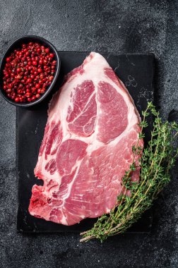 Mermer tahtada çiğ etten yapılmış domuz boyunlu biftek ve otlar. Siyah arka plan. Üst görünüm