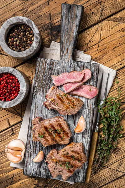 Pečené v BBQ jehněčích žebírkách steaky, kotlety na dřevěné desce s bylinkami. Dřevěné pozadí. Horní pohled — Stock fotografie