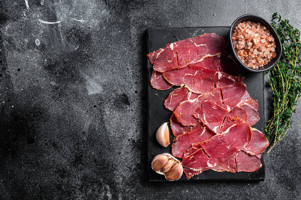Sliced Pastrami roasted beef meat with herbs. Black background. Top view. Copy space