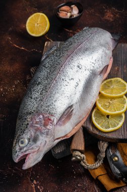 Tam alabalık, ahşap bir tahtanın üzerinde kekik ve limonla çiğ balık. Karanlık arka plan. Üst görünüm