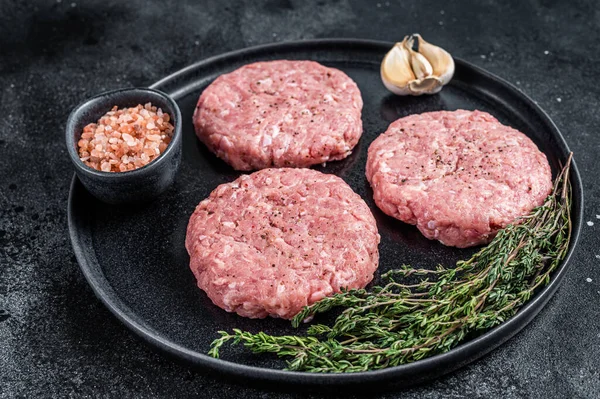 Raw chicken turkey patty, minced meat cutlets on a plate with thyme. Black background. Top view