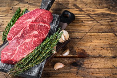 Tahta bir kasap tahtasında çiğ omuz üstü bıçaklı biftek ve otlar. Ahşap arka plan. Üst Manzara. Boşluğu kopyala