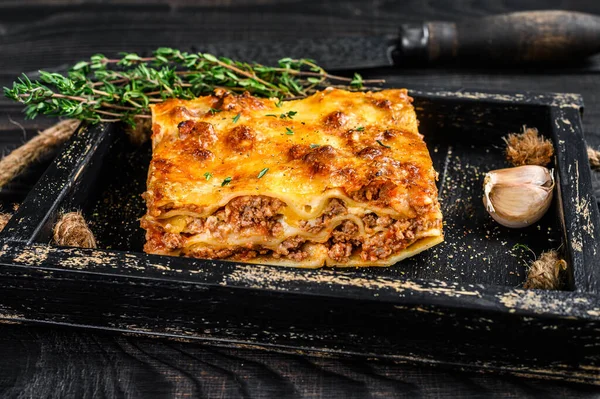 Portion of Lasagna with mince beef meat and tomato bolognese sauce in a wooden tray. Black wooden background. Top view — Stock Photo, Image