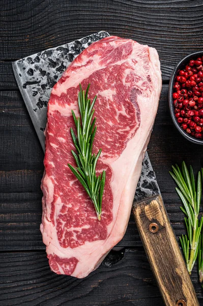 Bifteck de boeuf cru new york sur un hachoir à viande de boucher. Fond en bois noir. Vue du dessus — Photo