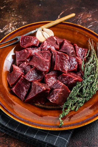 Cut Beef or veal raw heart in a rustic plate with herbs. Dark background. Top View