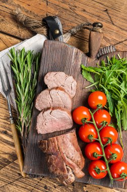 Kızarmış dana filetosu, ahşap tahtada dilimlenmiş biftek ve garnitür. Ahşap arka plan. Üst görünüm