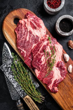 Tahta kesme tahtasının üzerinde kasap eti biftekleri, çiğ biftek. Siyah arka plan. Üst görünüm