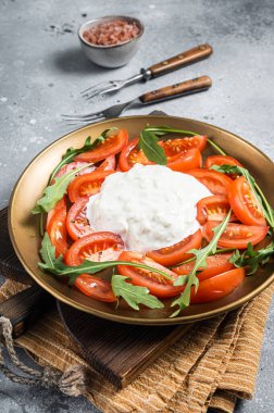 İtalyan peynirli stracciatella burrata tabakta taze domates ve roka. Gri arka plan. Üst görünüm