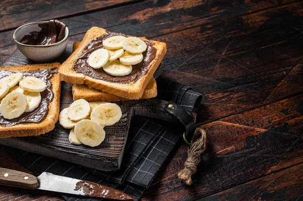 Tostadas de pan con plátanos y crema de chocolate sobre tabla de madera. Fondo de madera. Vista superior. Copiar espacio — Foto de Stock