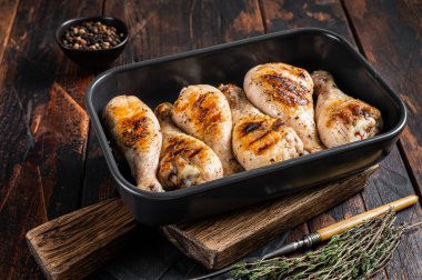 Pişmiş tavuk budu budu, otlarla dolu bir kabın içinde. Ahşap arka plan. Üst görünüm