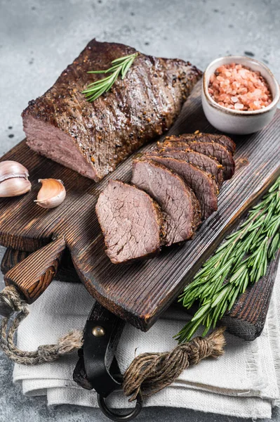 Pečeme a krájíme hovězí steak na dřevěné desce s bylinkami. Šedé pozadí. Horní pohled — Stock fotografie