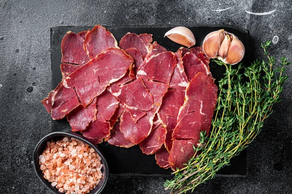 Viande de bœuf rôtie Pastrami tranchée avec des herbes. Fond noir. Vue du dessus — Photo