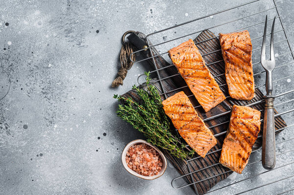 Grilled salmon fillets steaks with salt pepper and herb on grill. Gray background. Top view. Copy space