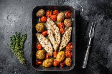 Kızarmış halibut balığı bifteği, domates ve patates. Siyah arka plan. Üst görünüm