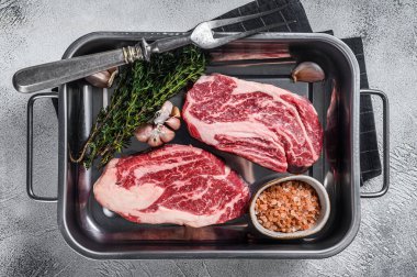 Çelik mutfak tepsisinde pişmemiş çiğ çiğ göz yuvarlama bifteği. Gri arka plan. Üst görünüm