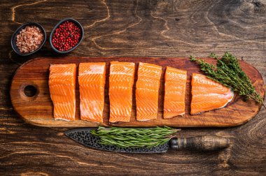 Dilimlenmiş somon filetosu, kekik ve biberiyeli çiğ balık eti. Ahşap arka plan. Üst görünüm