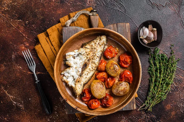 Baked halibut fish with roasted tomato and potato in wooden plate. Dark background. Top view — Stockfoto