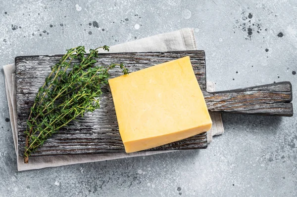 Hartkäse mit Messer auf Holzschneidebrett. Parmesan. Grauer Hintergrund. Ansicht von oben — Stockfoto