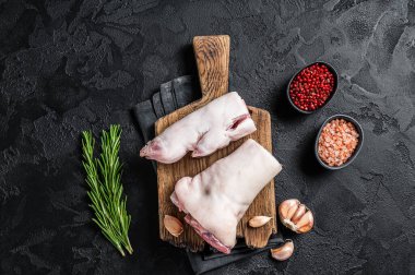 Çiğ domuz budu ya da toynak, kesme tahtasındaki ayaklar. Siyah arka plan. Üst görünüm