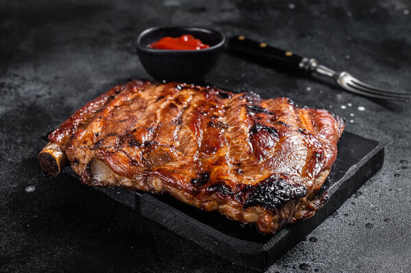 Full rack of BBQ grilled pork spare ribs on a marble board. Black background. Top view.
