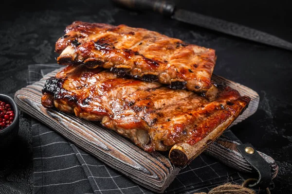 Pilha de costelas de porco grelhadas em molho de churrasco em uma tábua de cortar. Fundo preto. Vista superior — Fotografia de Stock